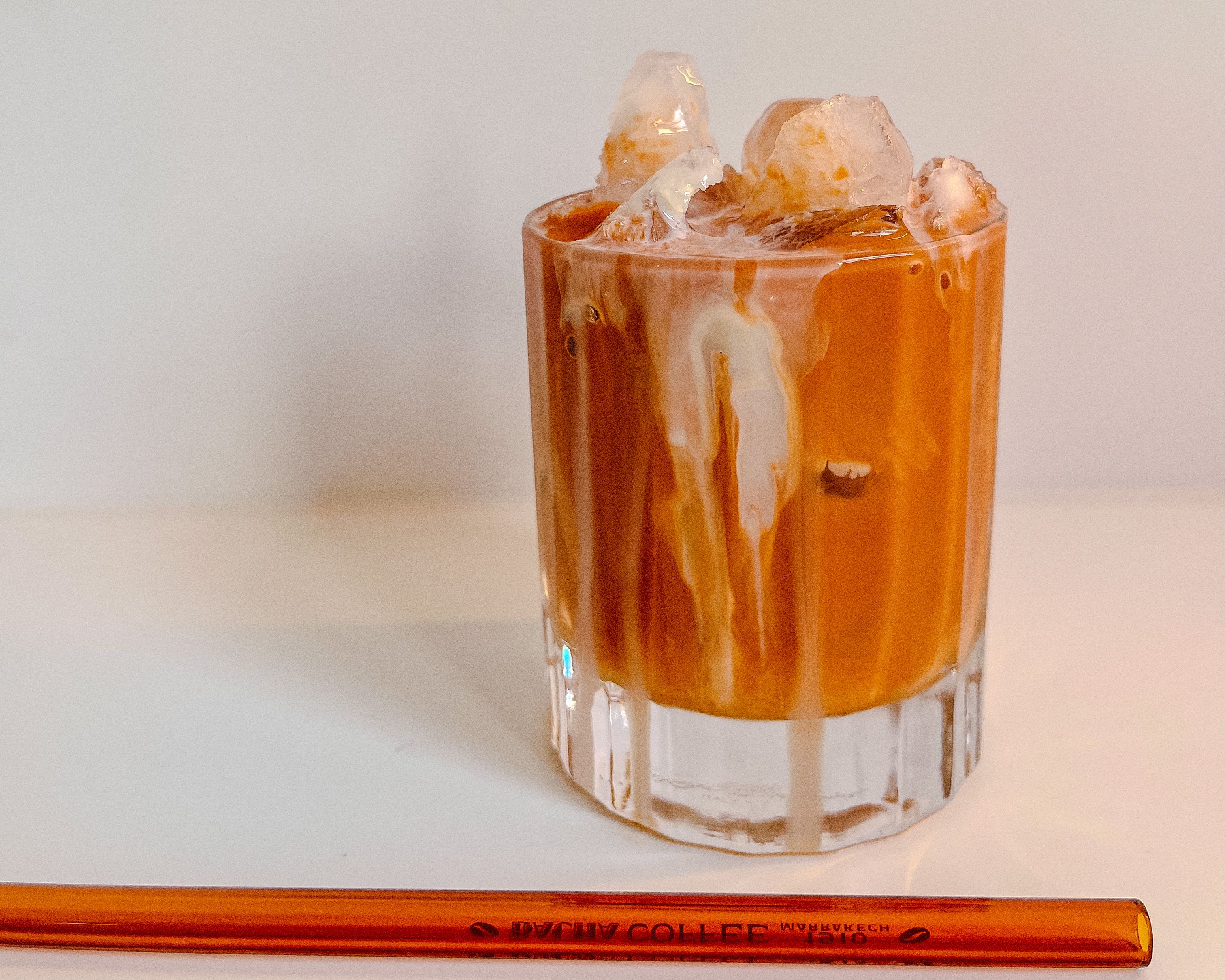 Authentischer Cha Yen - Thai Ice Tea mit süsser Kondensmilch und Eiswürfeln, serviert im Glas mit oranger Trinkhalm.
