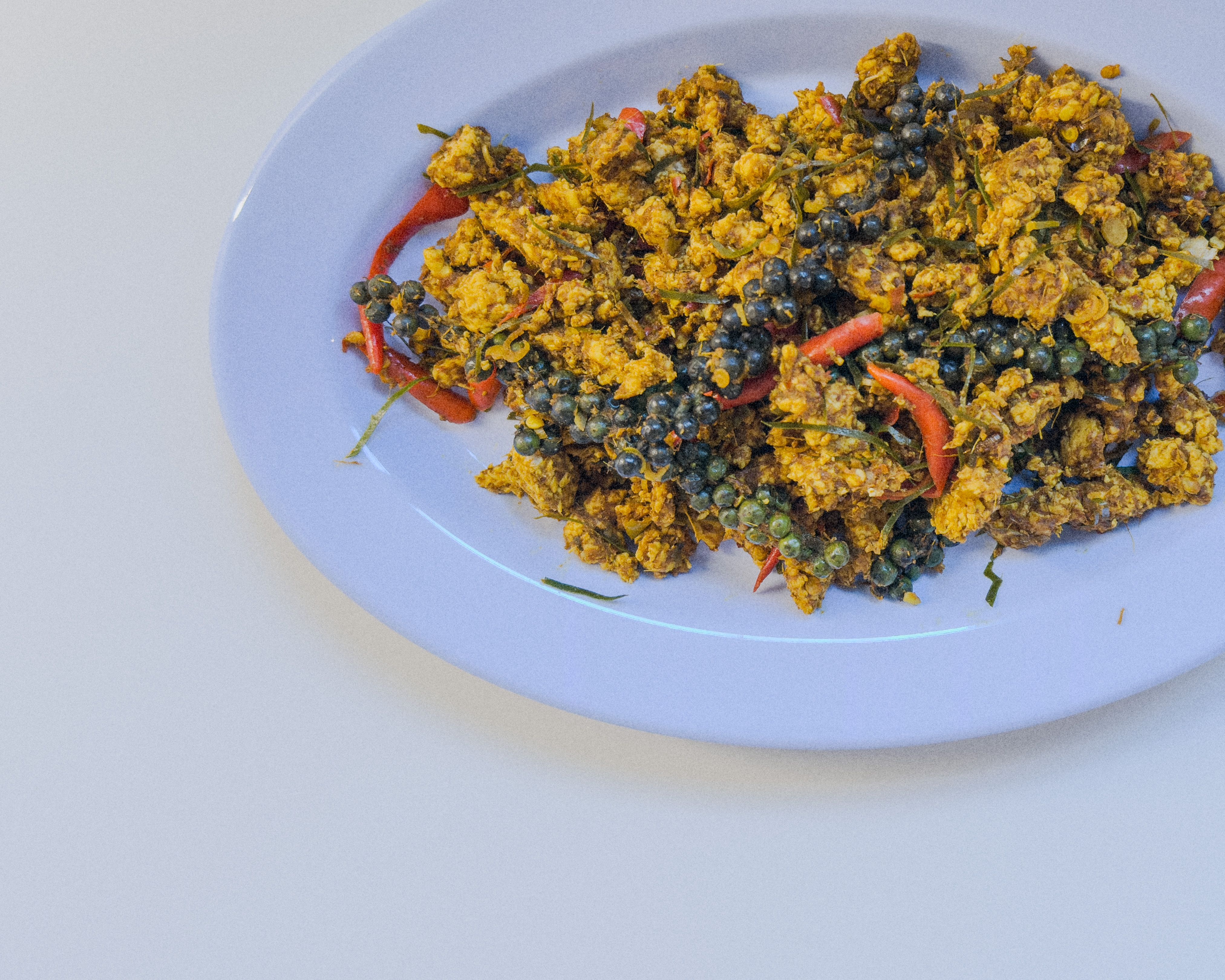 Authentisches Khua Kling – südthailändisches, trockenes Curry mit Schweinefleisch auf einem blauen Teller serviert