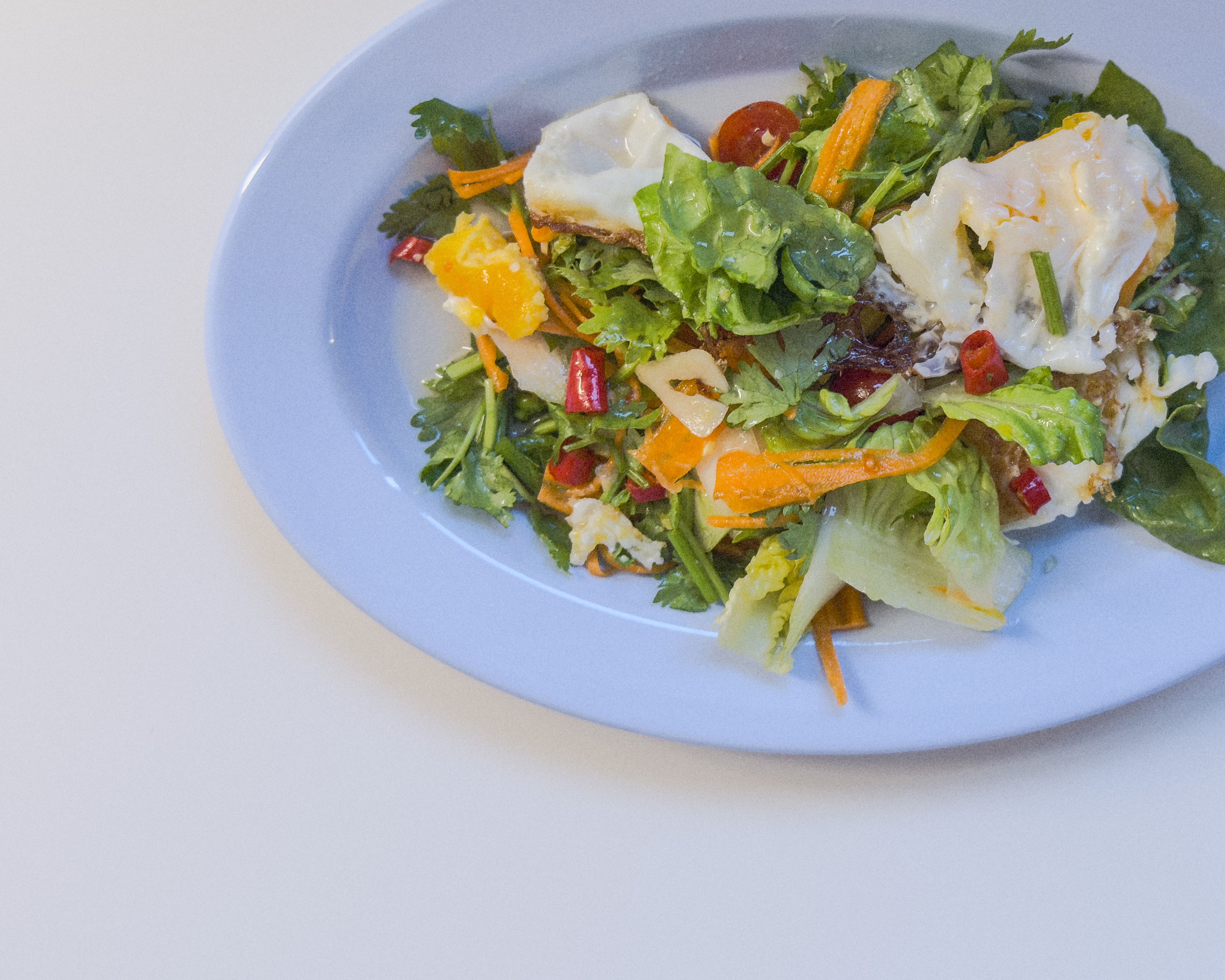 Authentischer Yum Khai Dao - thailändischer Salat mit knusprig gebratenem Ei, Tomaten, Zwiebeln, Sellerie und Koriander auf blauem Teller.