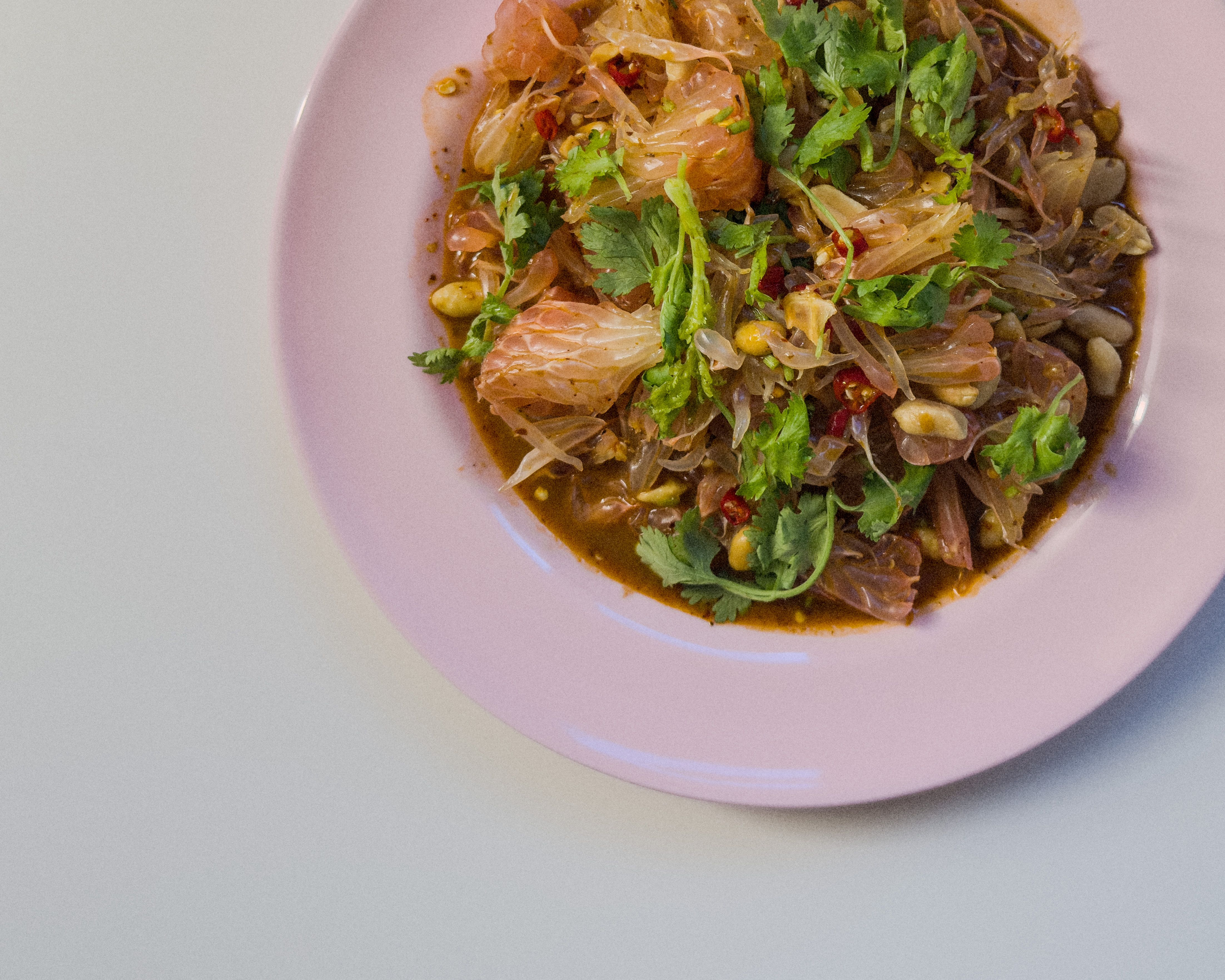Authentischer Yam Som O – thailändischer Pomelosalat mit Minze, gerösteter Kokosnuss, Erdnüssen und Chili, serviert auf pinkem Teller.