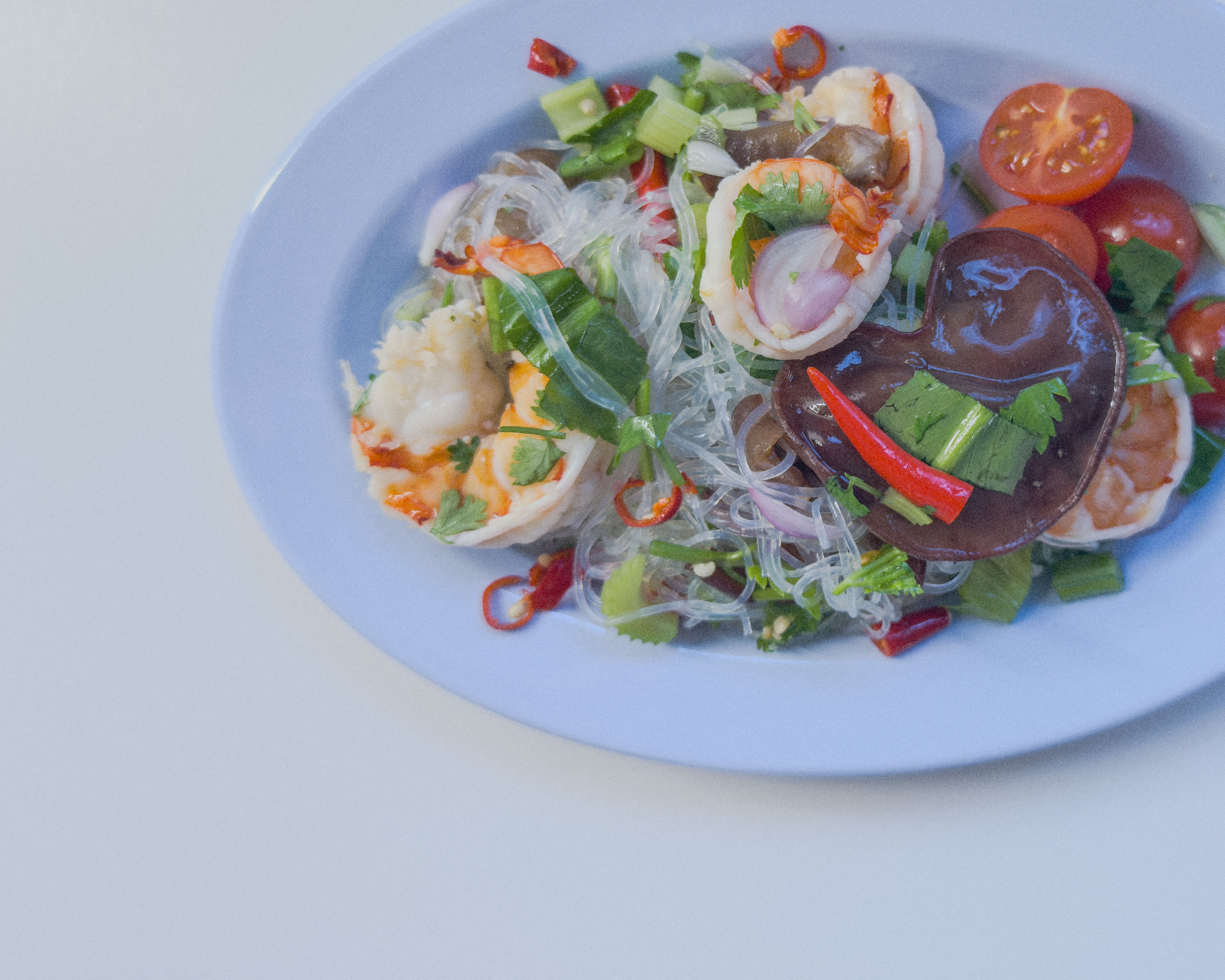 Authentischer Yum Tale – thailändischer Meeresfrüchtesalat mit Garnelen, Tomaten, Zwiebeln, Pilzen und Koriander auf blauem Teller.